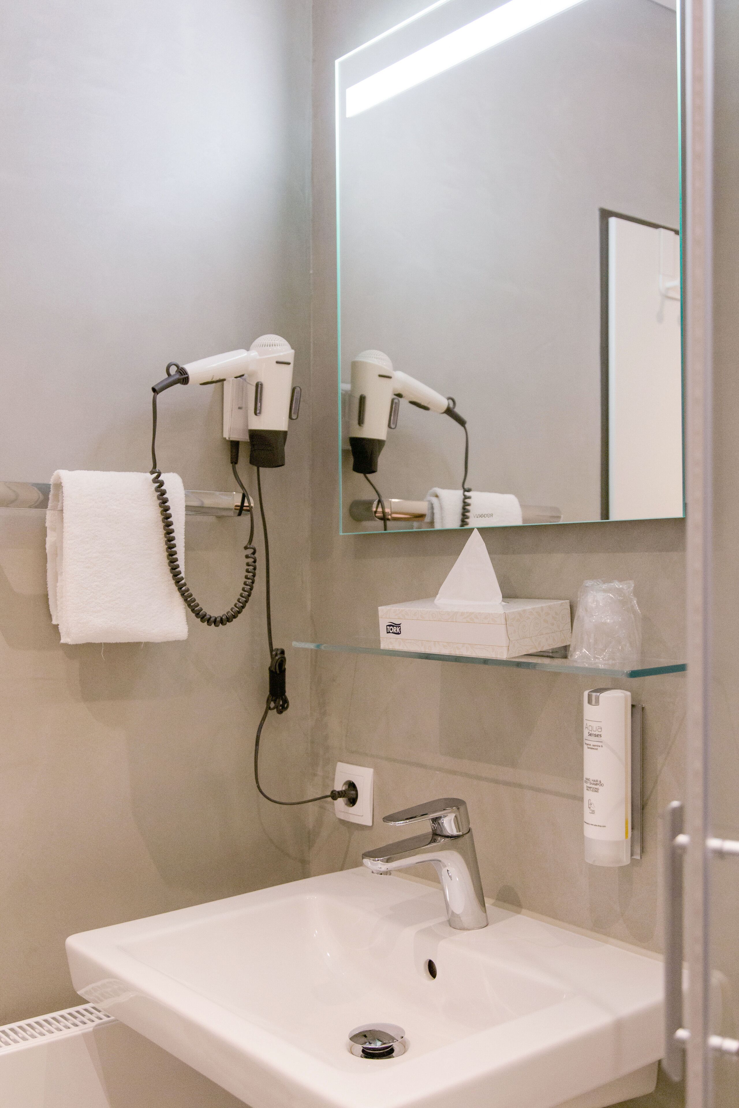 A bathroom with a white sink, a mirror, and two hair dryers mounted on the wall.