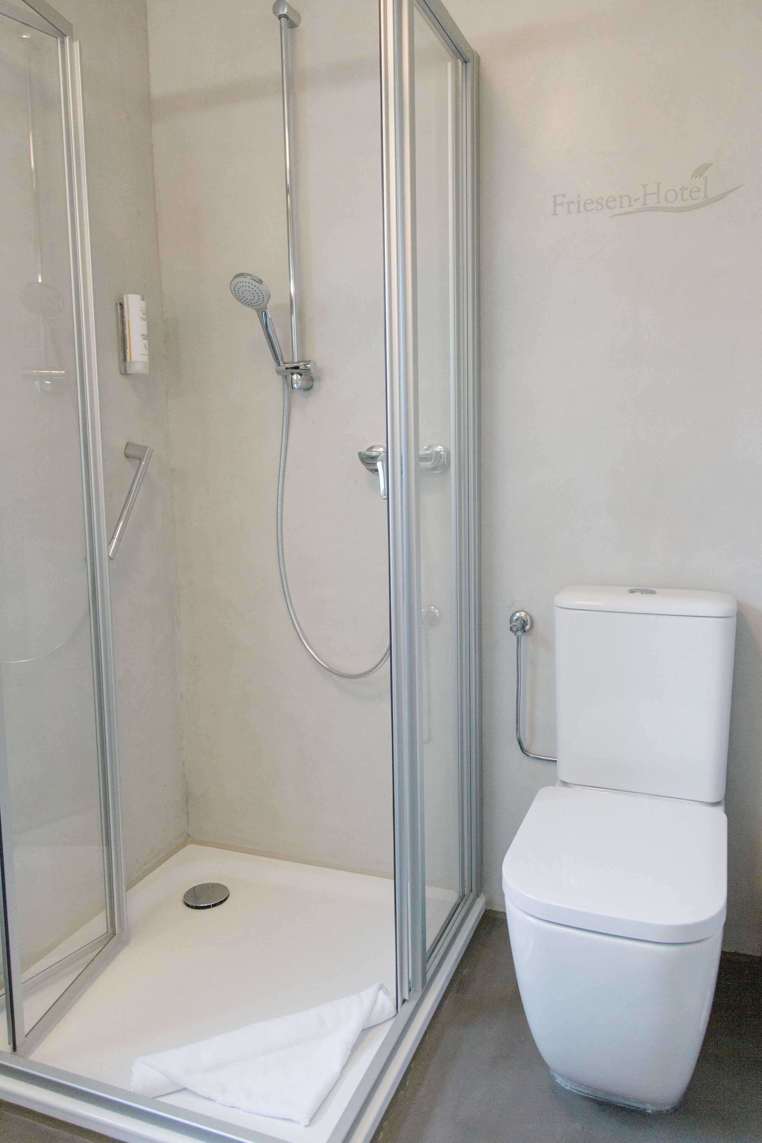 Un baño moderno con ducha envuelta en vidrio, inodoro blanco y secamanos visible.