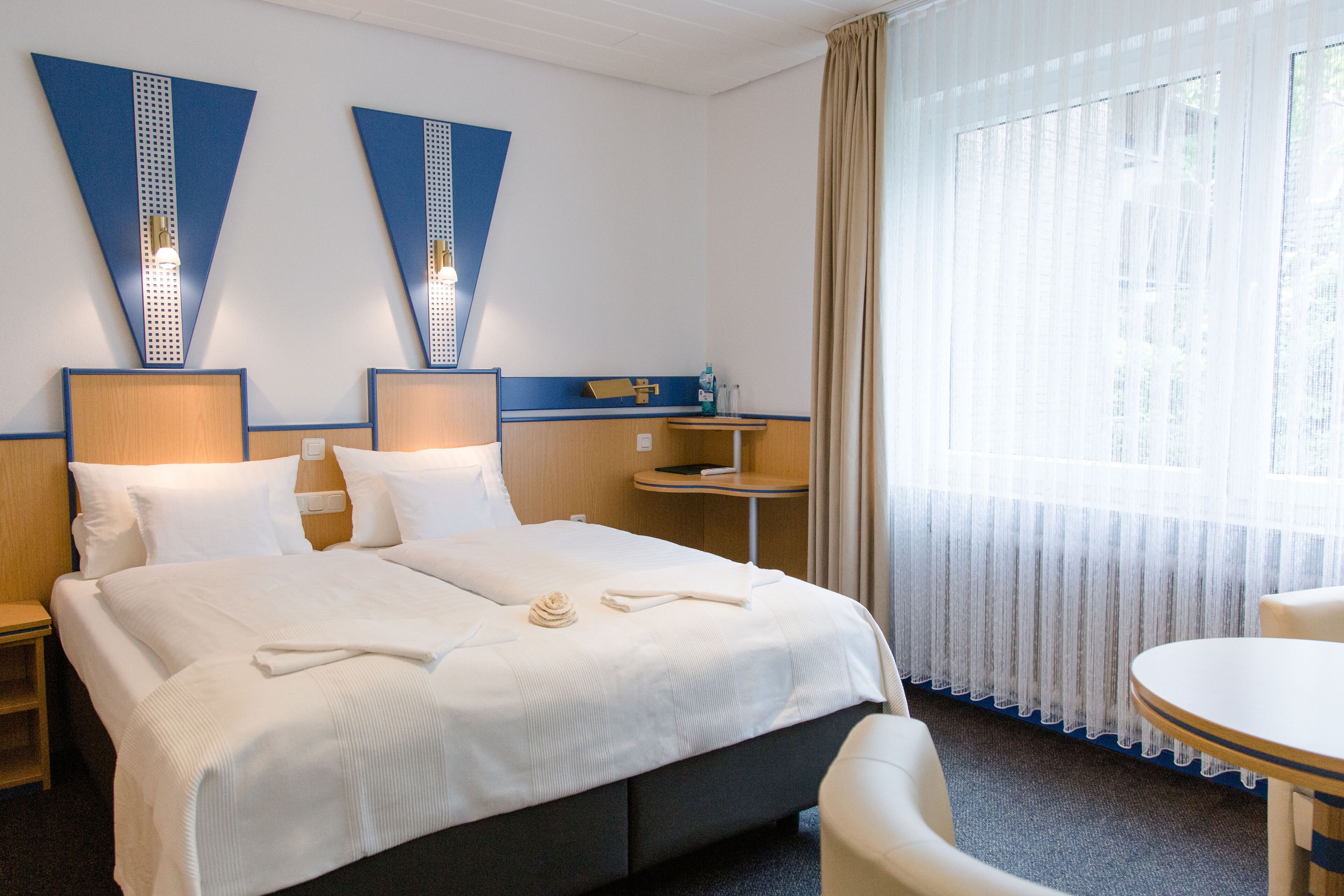 A hotel room with a large bed, two bedside tables, a small table, and a chair.