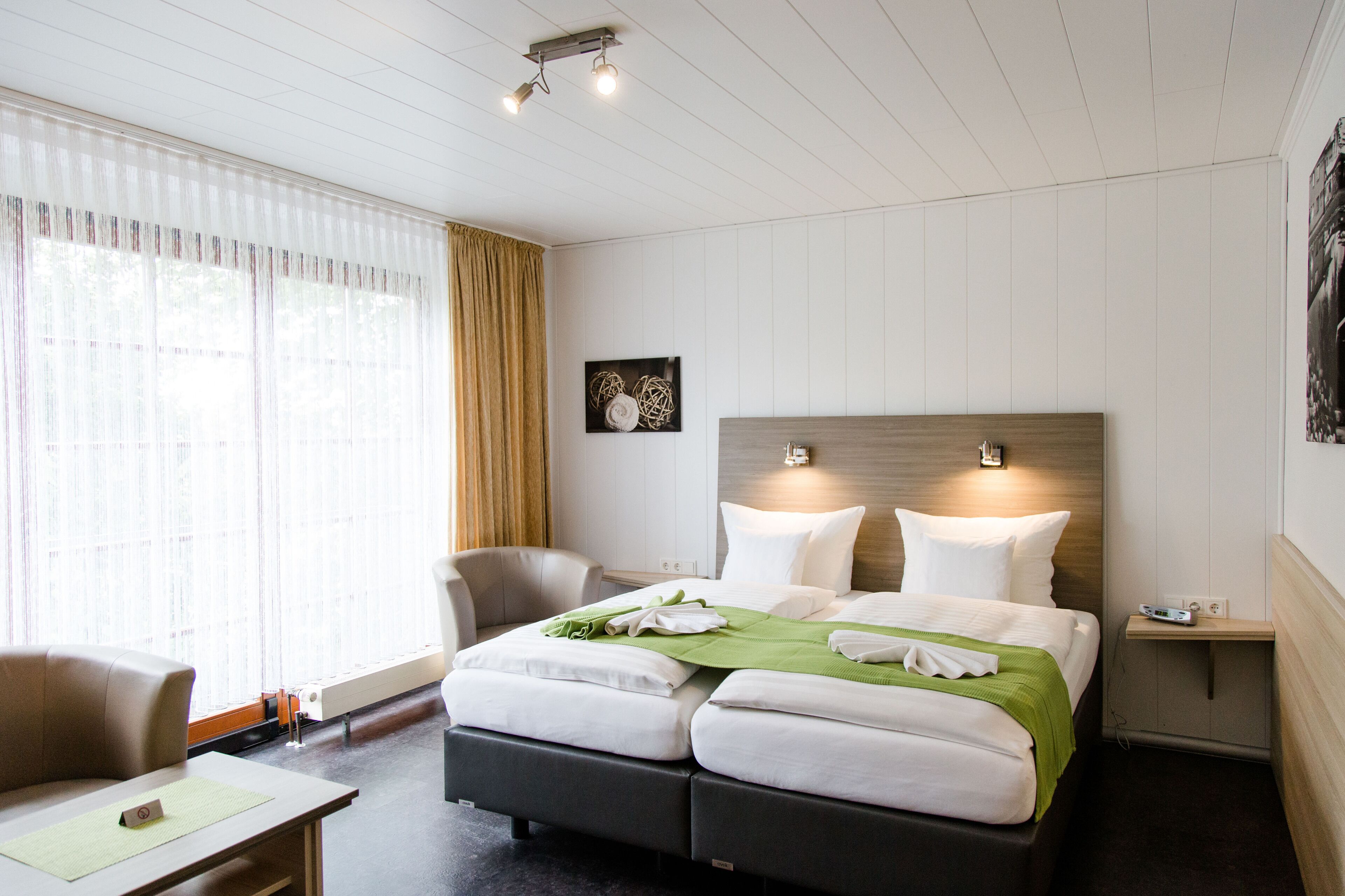 A hotel room with a large bed, a chair, a desk, and a nightstand.