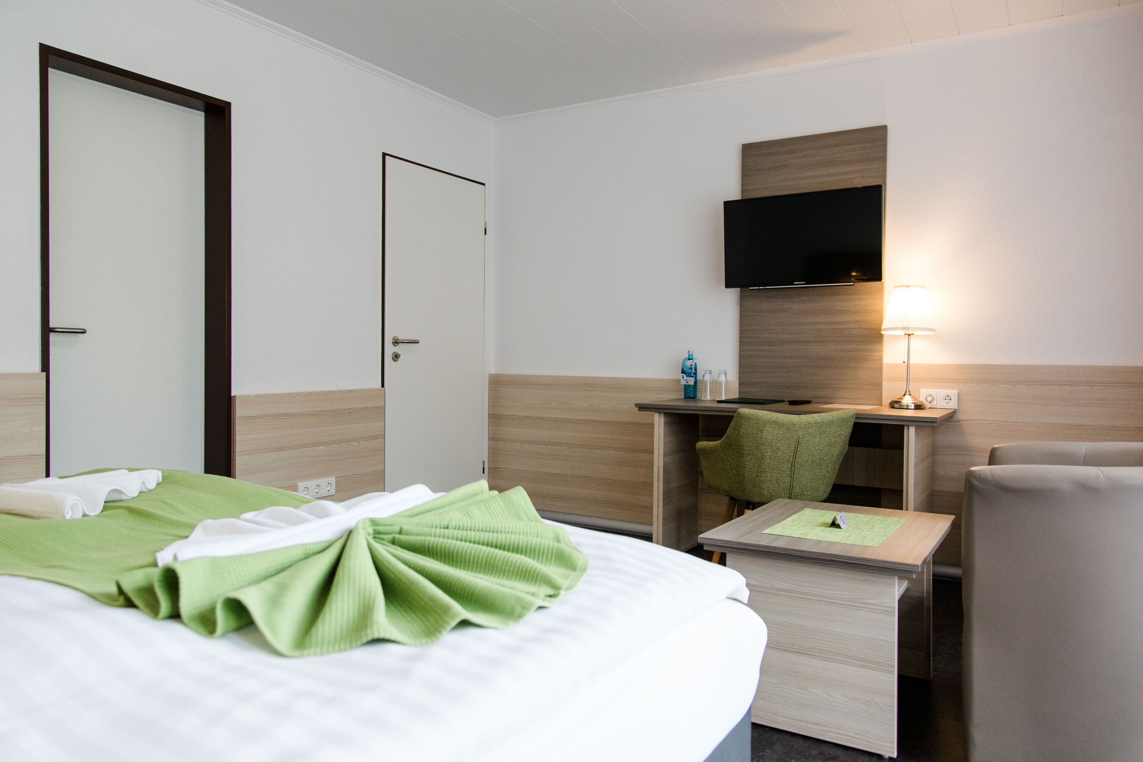 A hotel room with a bed, a desk, a chair, a television, and a lamp.