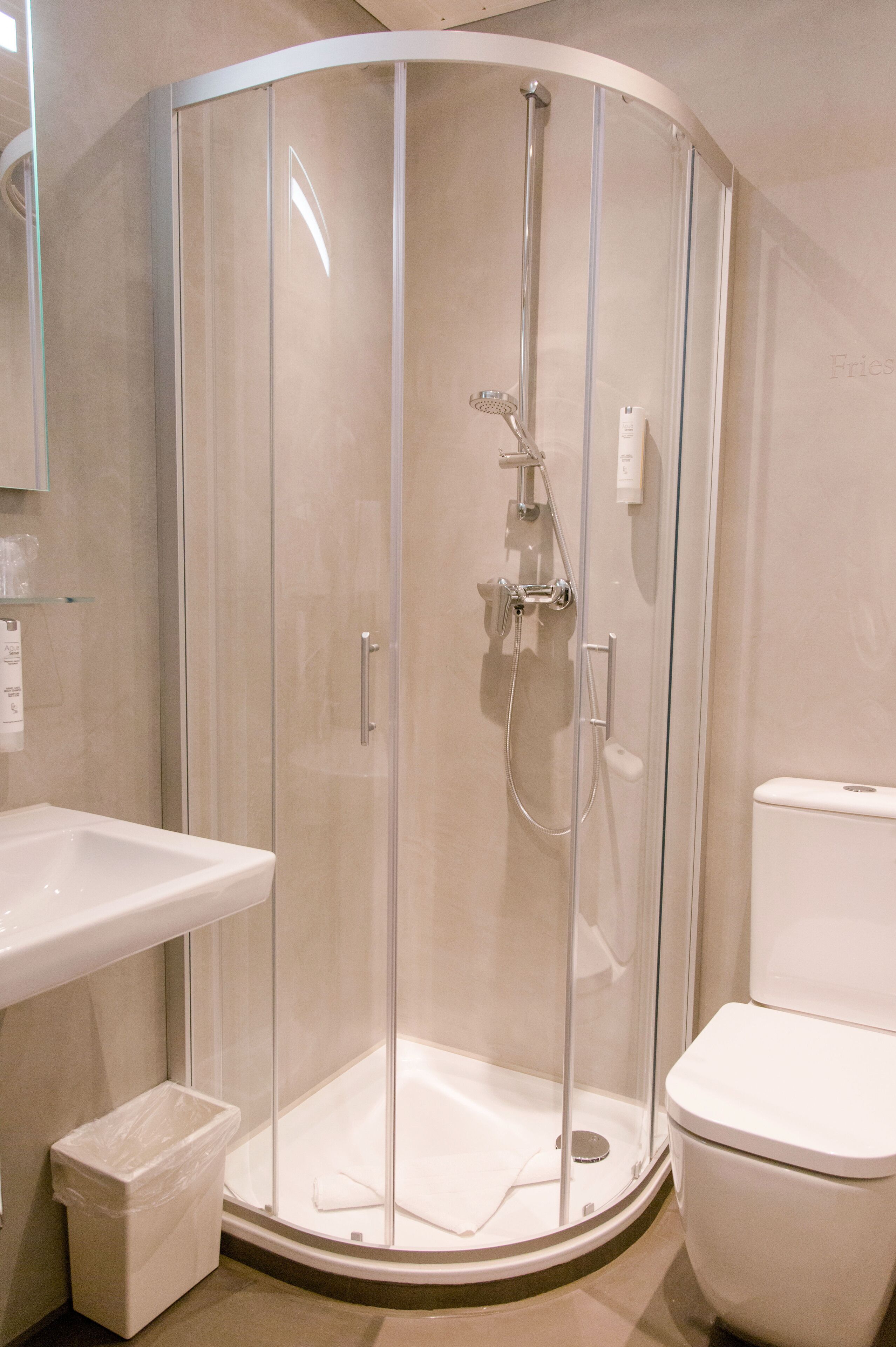 Een douchecabine met hoekopstelling, een glazen deur, een witte wastafel en een toilet.