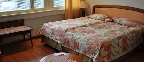 Habitación de hotel con cama, un banco, una mesita y una ventana con persianas.