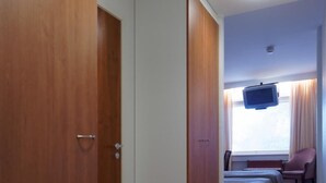 A hallway with wooden flooring leading to a room with two beds, a television, and a chair. - Laitilan Kievari (Laitila)