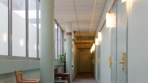 A hallway with wooden chairs and tables, a plant, and doors with light fixtures. - Laitilan Kievari (Laitila)
