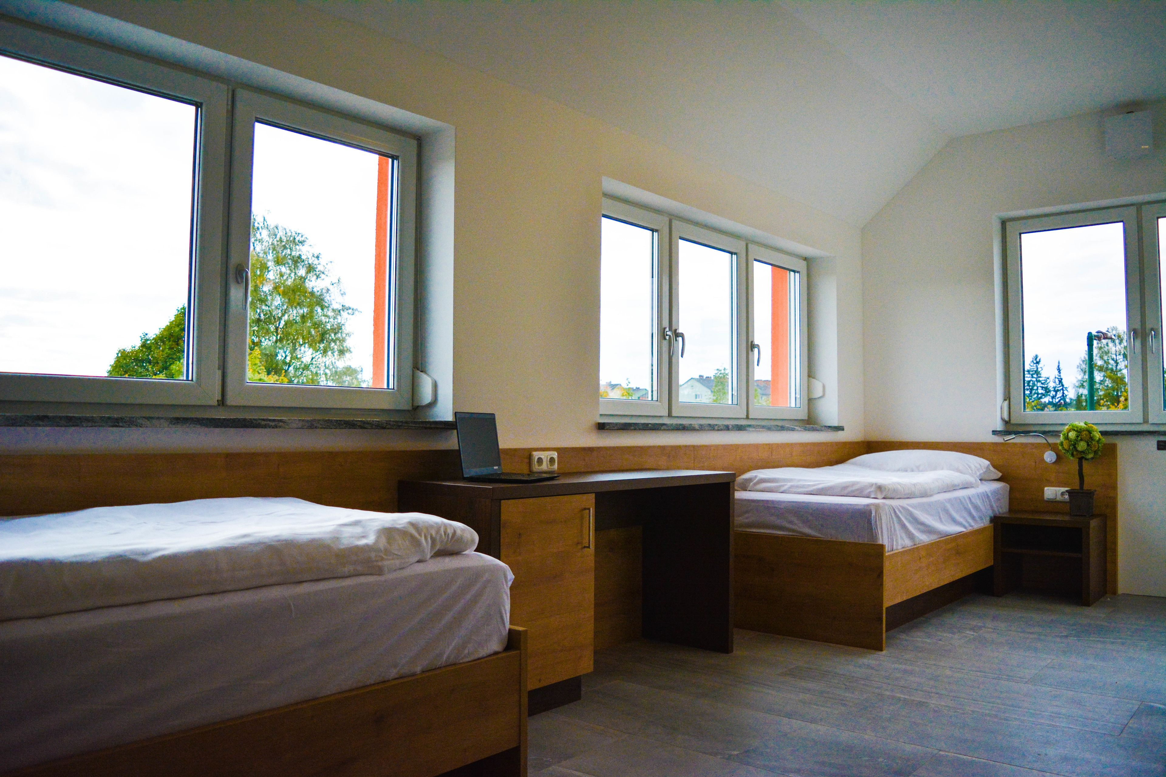 Ein Schlafzimmer mit zwei Einzelbetten, einem Holztisch und einem Fenster mit Blick auf Bäume.