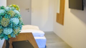 Een hotelkamer met een houten bureau, een laptop, een potplant, een bed en een aan de muur bevestigde televisie.