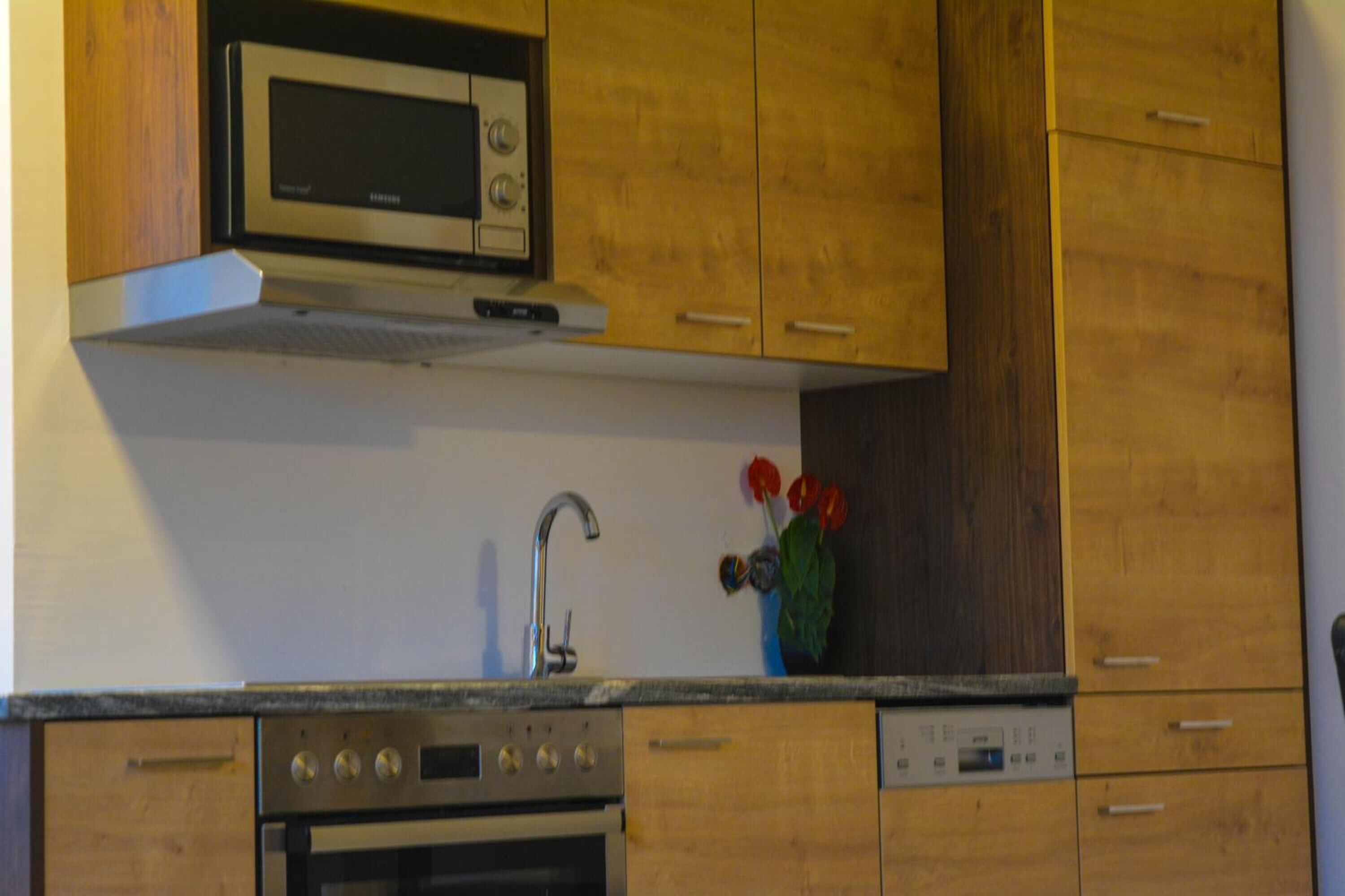 Una cocina con gabinetes de madera, un microondas de acero inoxidable, un horno empotrado, un lavavajillas y un fregadero.