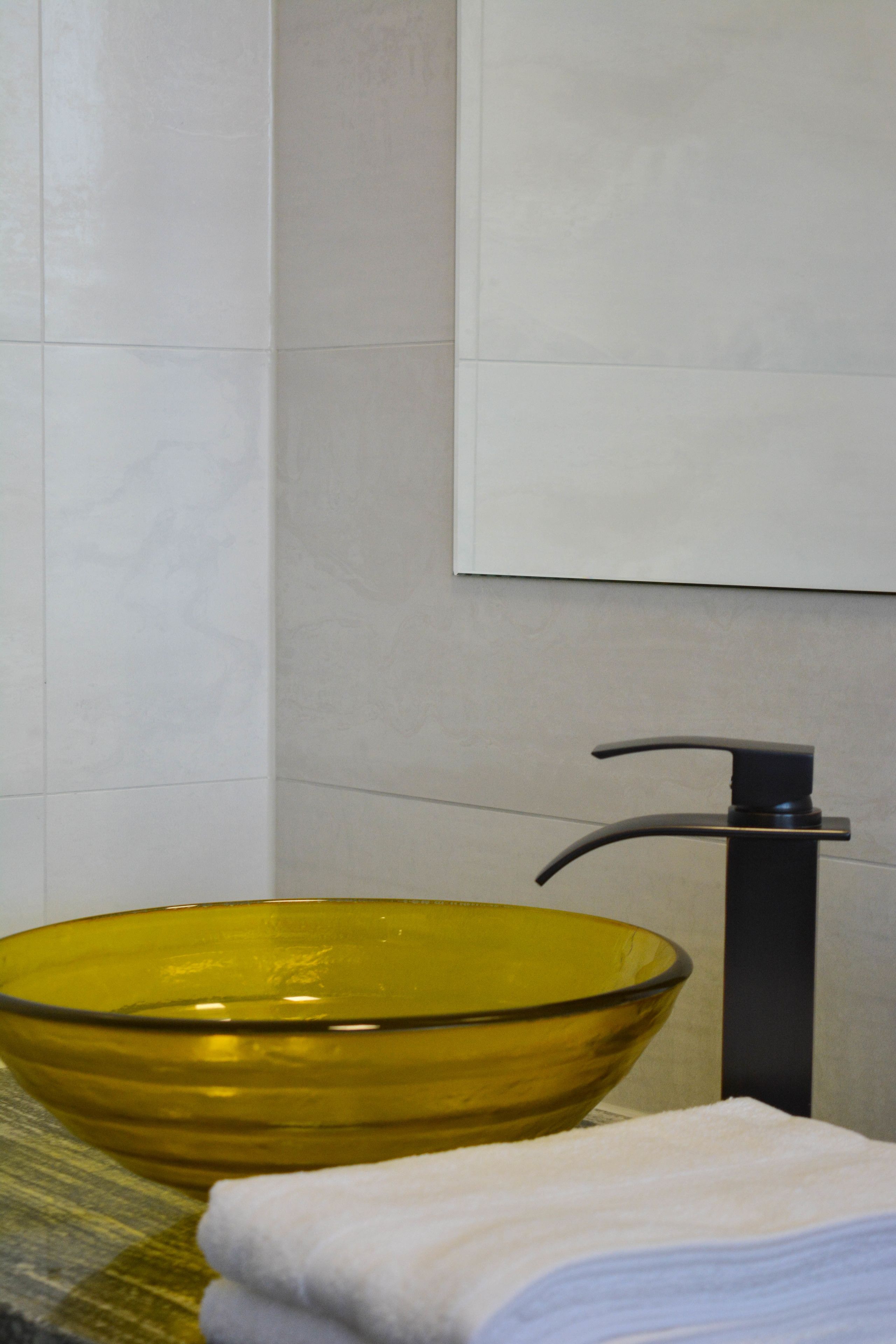 Une salle de bain avec un lavabo en verre jaune, un robinet noir et une serviette blanche.