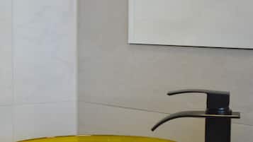 Une salle de bain avec un lavabo en verre jaune, un robinet noir et une serviette blanche.