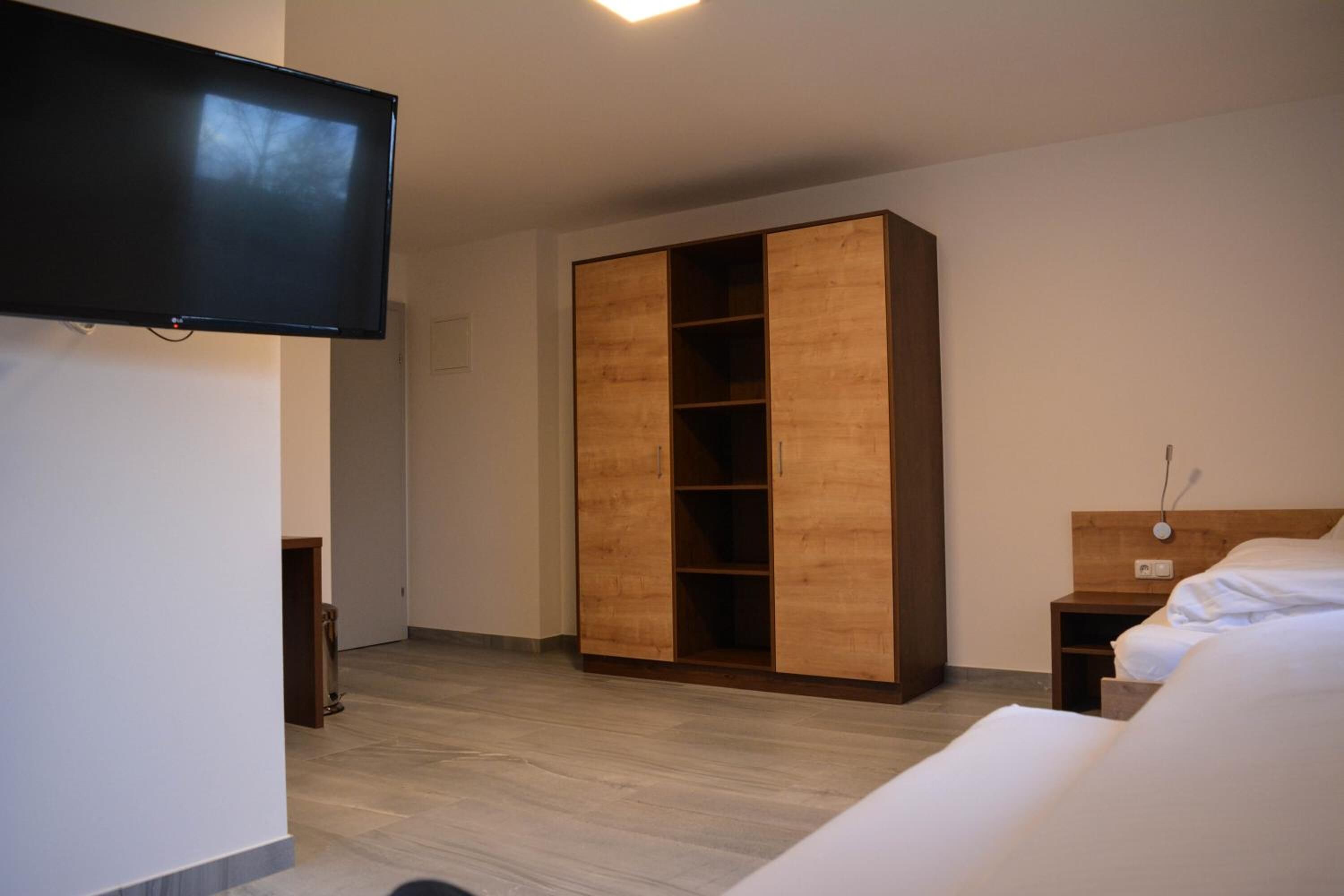 Un dormitorio con cama, armario de madera, mesita de noche y televisor de pared.