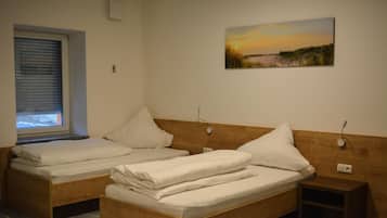 Una habitación con dos camas individuales, una mesita de noche, un velador, una ventana con persianas y un cuadro en la pared.