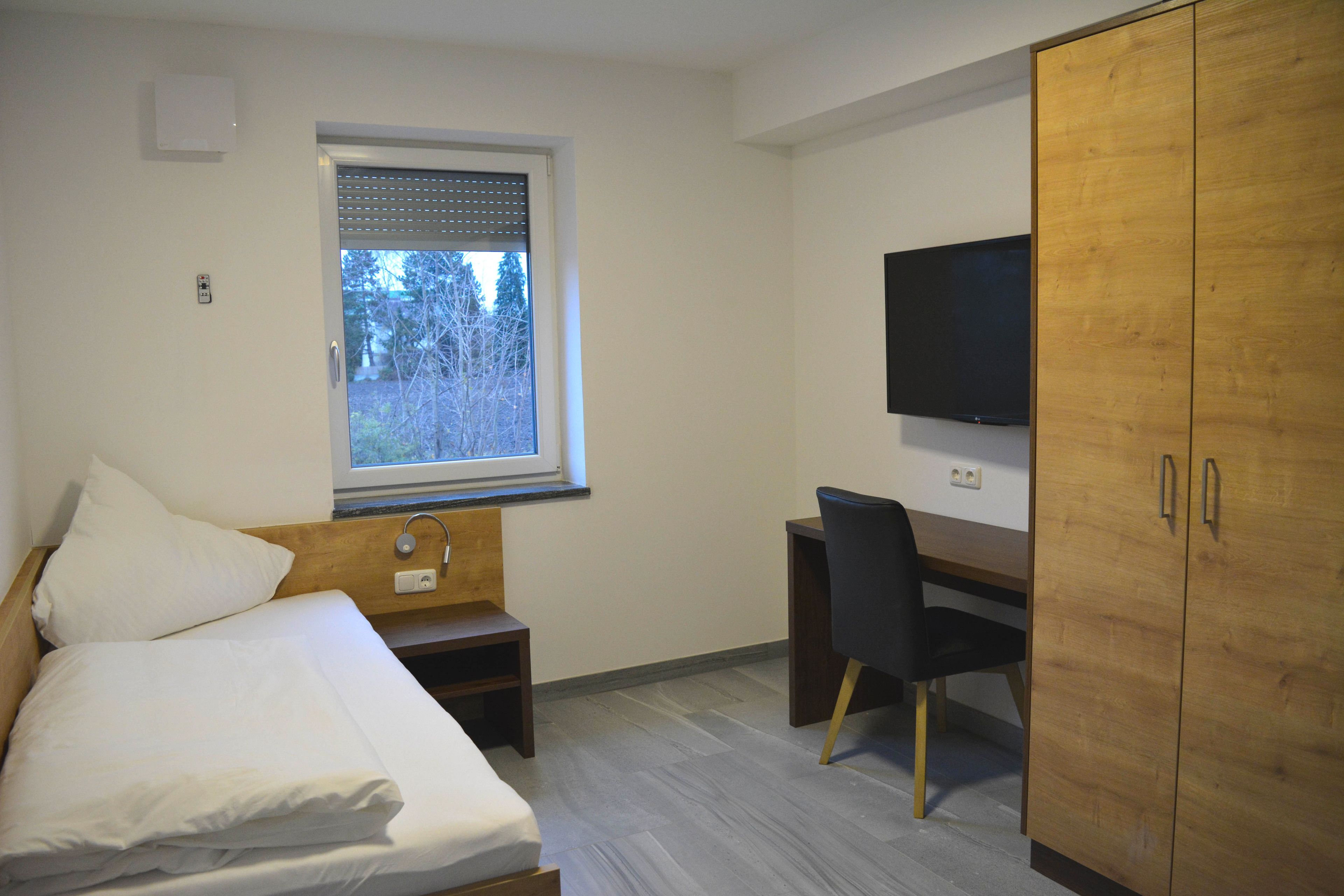 A bedroom with a bed, a desk, and a TV.