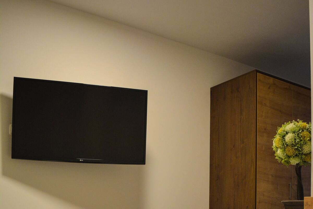 Ein Schlafzimmer mit einem Bett, einem an der Wand montierten Fernseher und einem Holzschrank.
