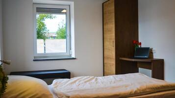 A bedroom with a bed, a window, a wooden wardrobe, and a laptop on a small table.