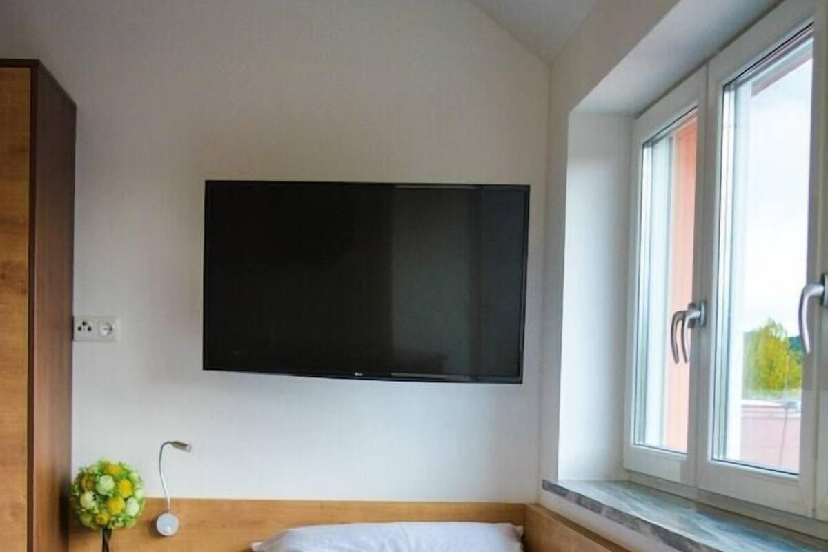 Ein Schlafzimmer mit einem Bett, einem Schreibtisch, einem an der Wand montierten Fernseher und einem Fenster.