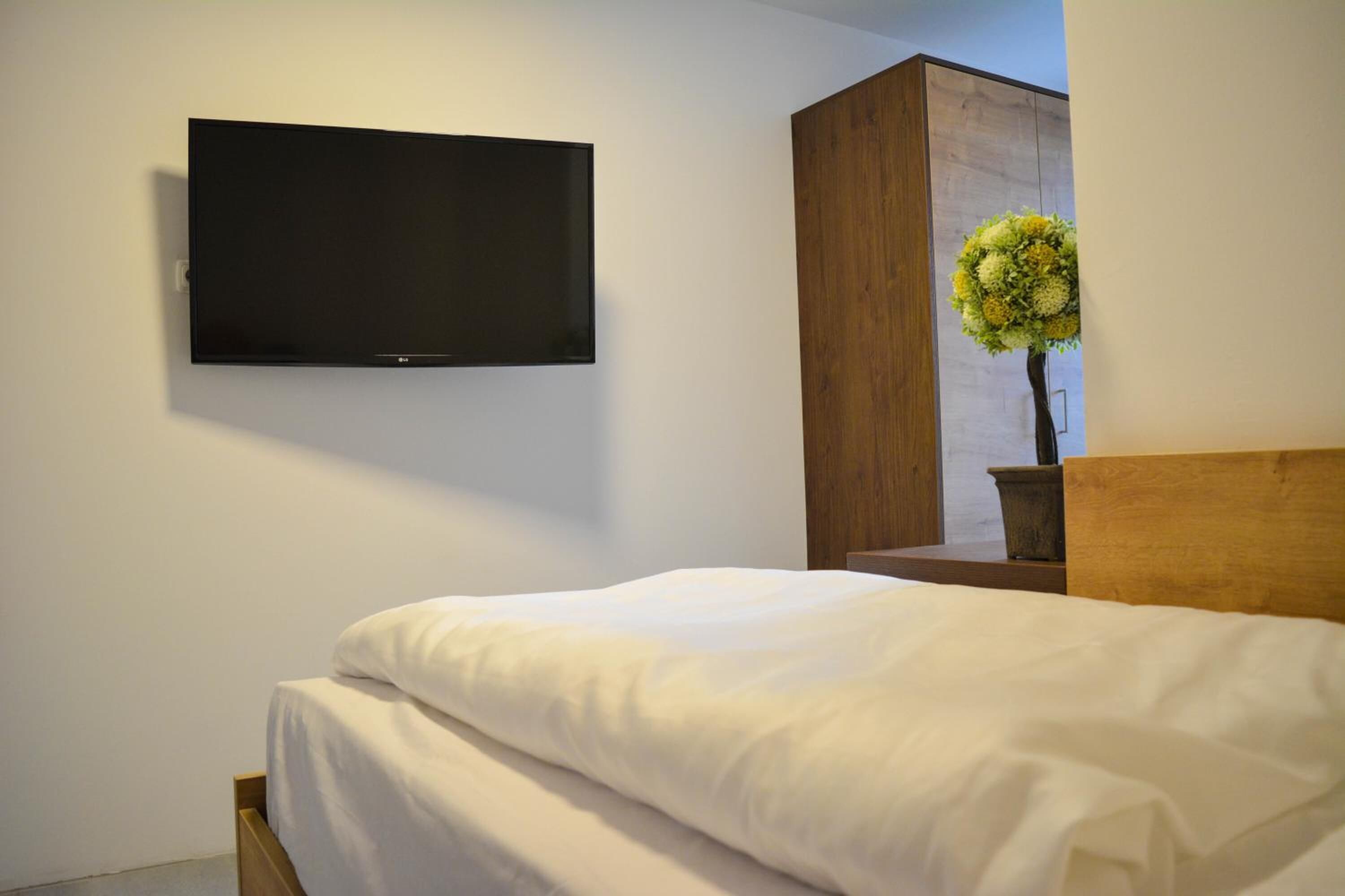 Un dormitorio con una cama, un televisor montado en la pared y un armario de madera.