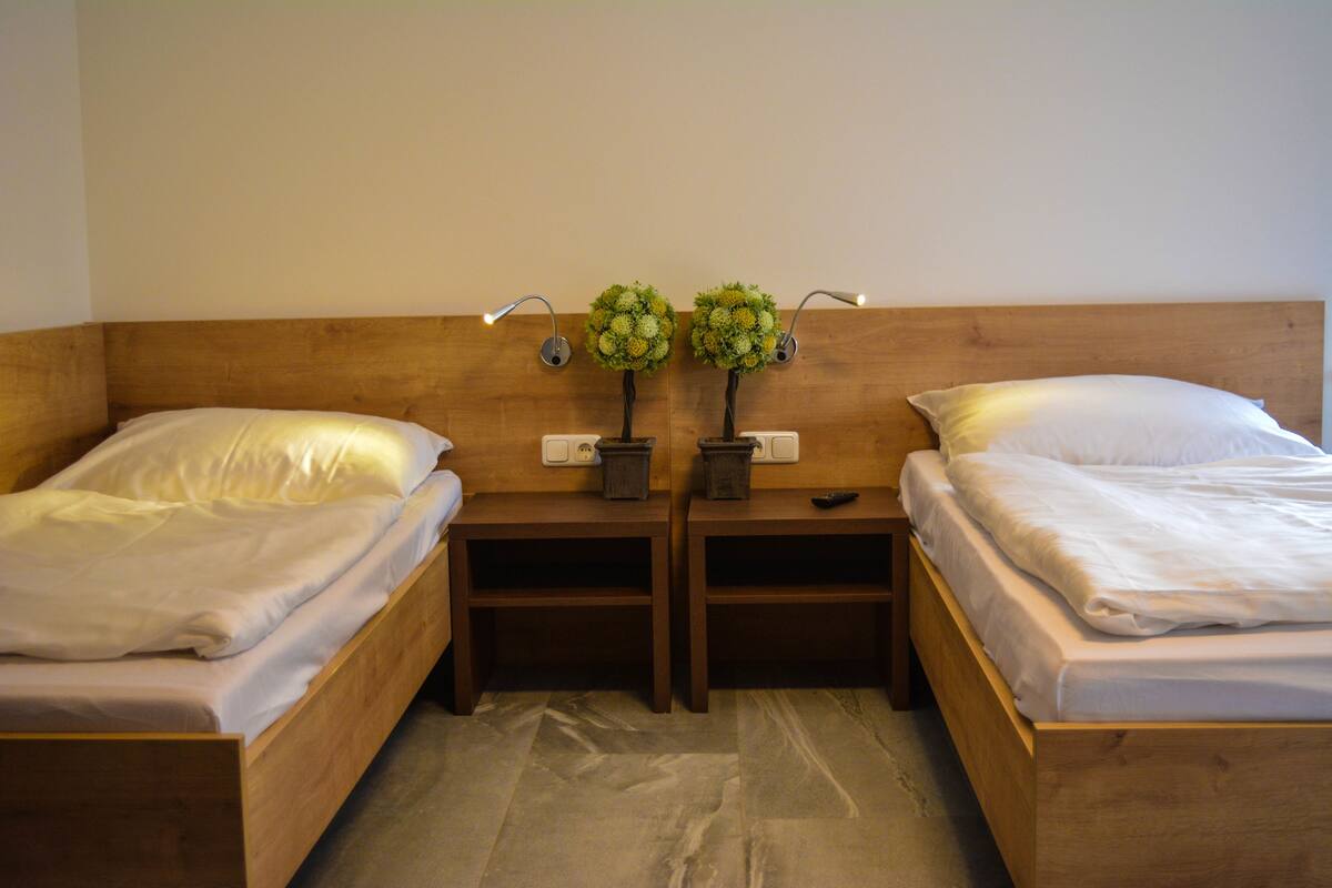 Ein Doppelzimmer mit zwei Einzelbetten, Holz-Kopfteilen, Nachttischen und zwei Wandlampen.
