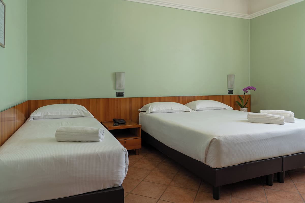 A hotel room with two single beds, a nightstand, a small table, and a wall-mounted lamp.