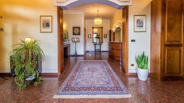 A hallway with a patterned rug, wooden doors, and framed pictures on the walls.