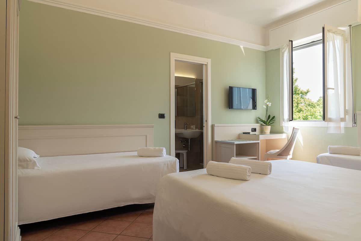 A hotel room with two beds, a bathroom, a desk with a computer, and a TV.