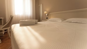 A hotel room with a large bed, a chair, a nightstand, and a window with curtains.