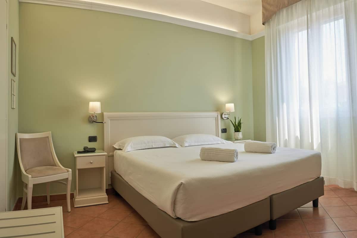A neatly arranged hotel room with a large bed, bedside lamps, a chair, and a small table with a plant.