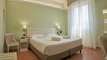 A neatly arranged hotel room with a large bed, bedside lamps, a chair, and a small table with a plant.