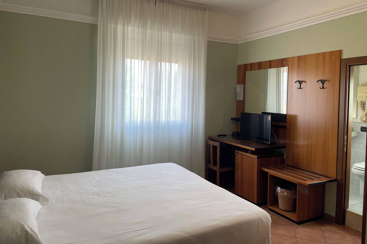 A hotel room with a bed, a desk with a computer, a mirror, and a wardrobe.