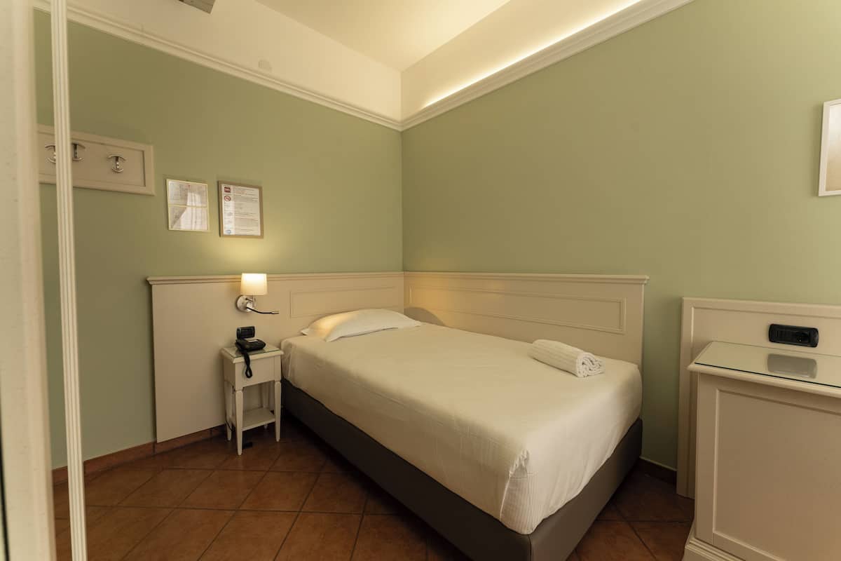 A neatly arranged hotel room with a single bed, bedside table, and a small desk.