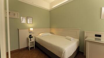 A neatly arranged hotel room with a single bed, bedside table, and a small desk.