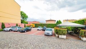 A parking area with several cars, a covered seating area, and a building with a yellow facade.