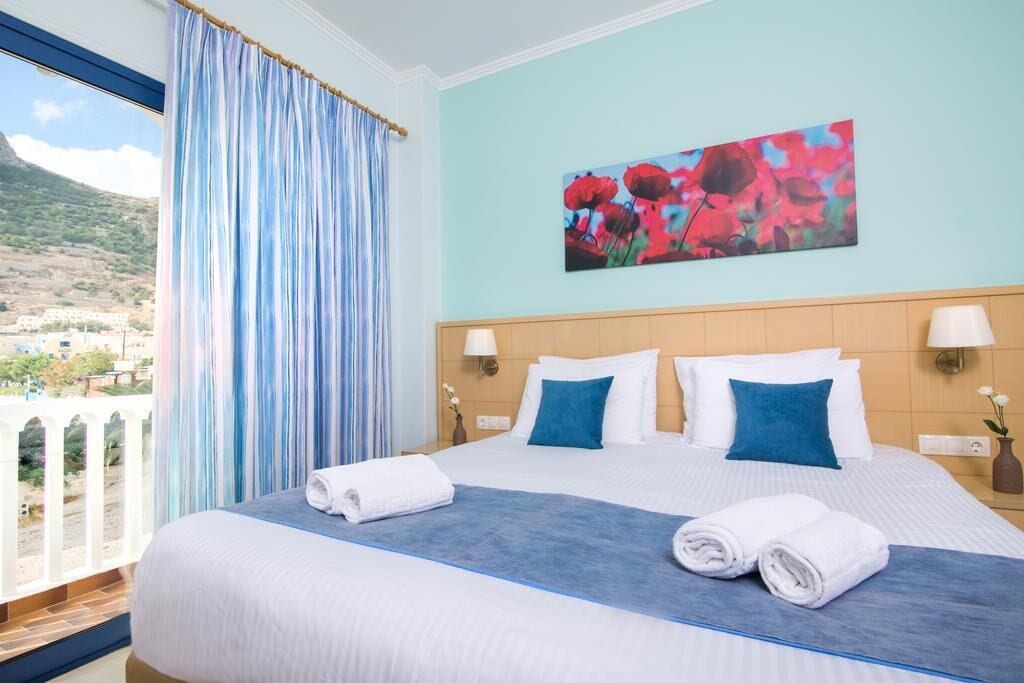 A hotel room with a large bed, two pillows, a painting, and a view of a mountainous landscape.