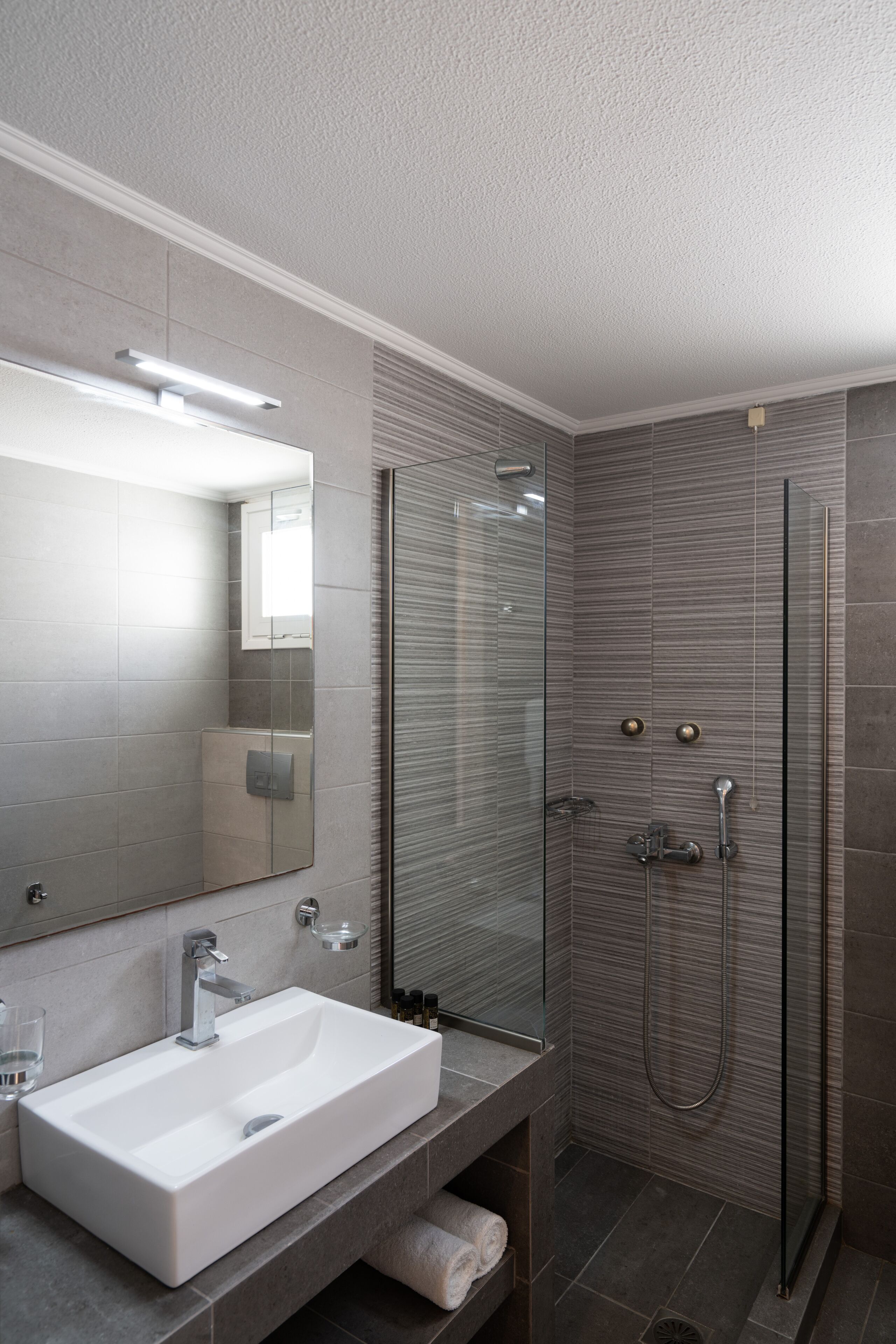 Une salle de bain moderne avec un lavabo rectangulaire, un grand miroir et une douche séparée par des parois en verre.