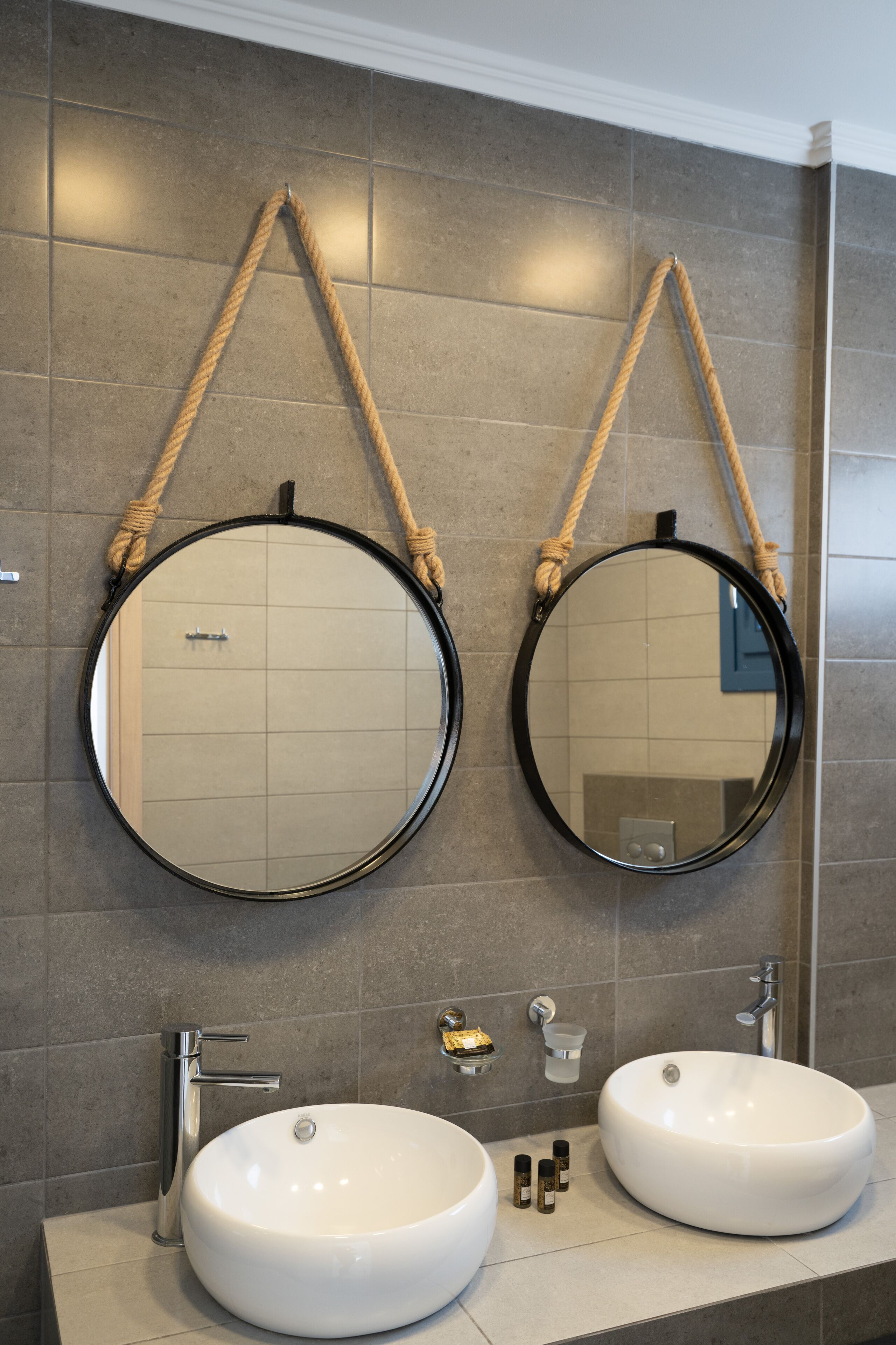 Un baño con dos espejos redondos colgados con cuerdas, un lavamanos doble y un diseño moderno.