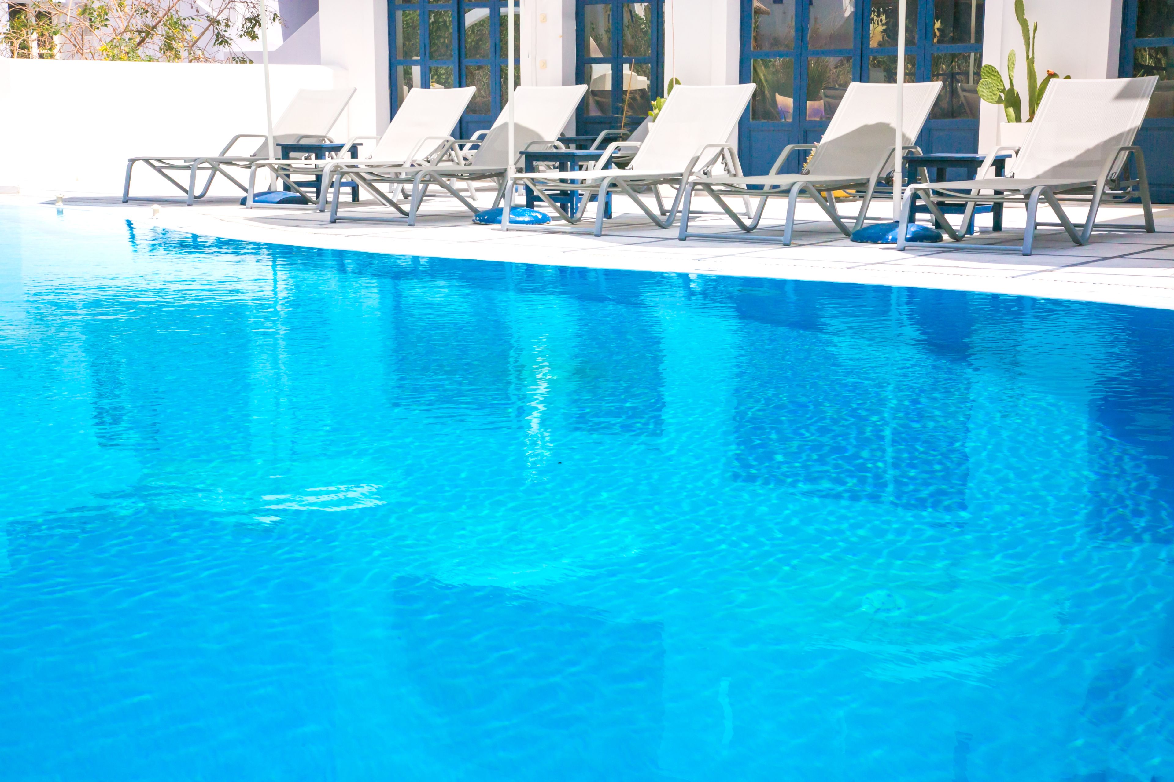 A swimming pool with clear blue water, surrounded by white lounge chairs and a white building with large windows.