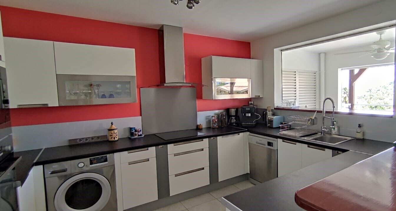 A modern kitchen with white cabinets, a black countertop, and a red accent wall.