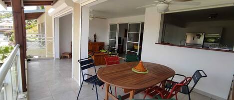 A covered outdoor dining area with a wooden table and chairs, a ceiling fan, and a view of the surrounding buildings.