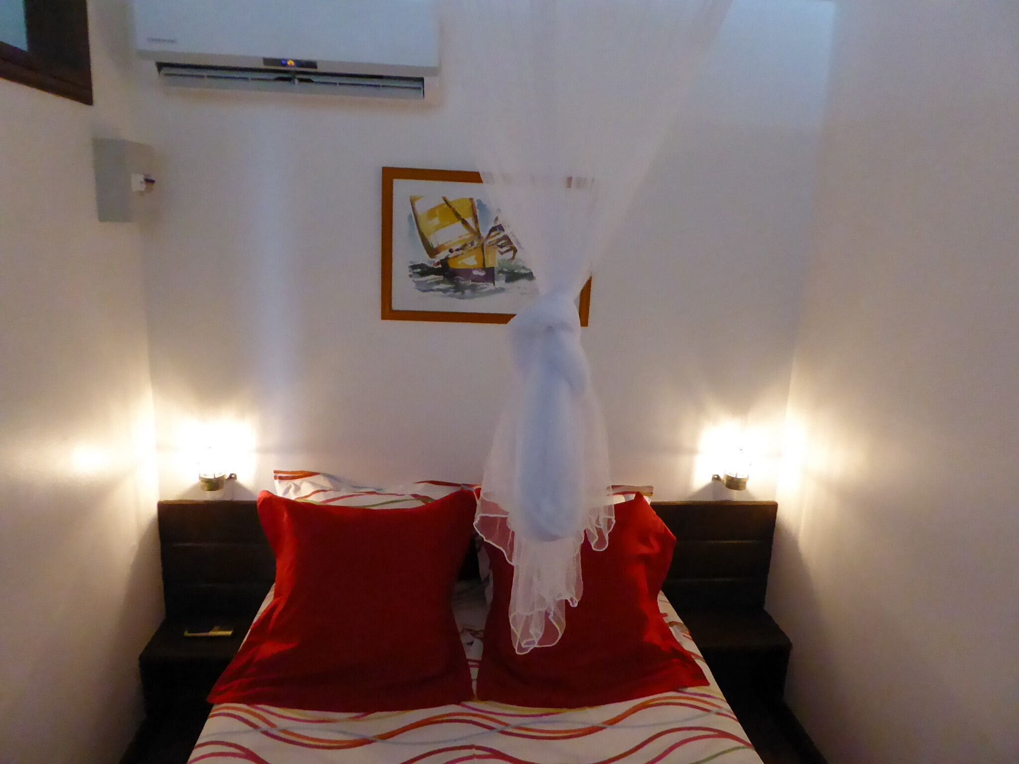 A bedroom with a bed, two nightstands, a wall-mounted air conditioner, and a framed picture on the wall.