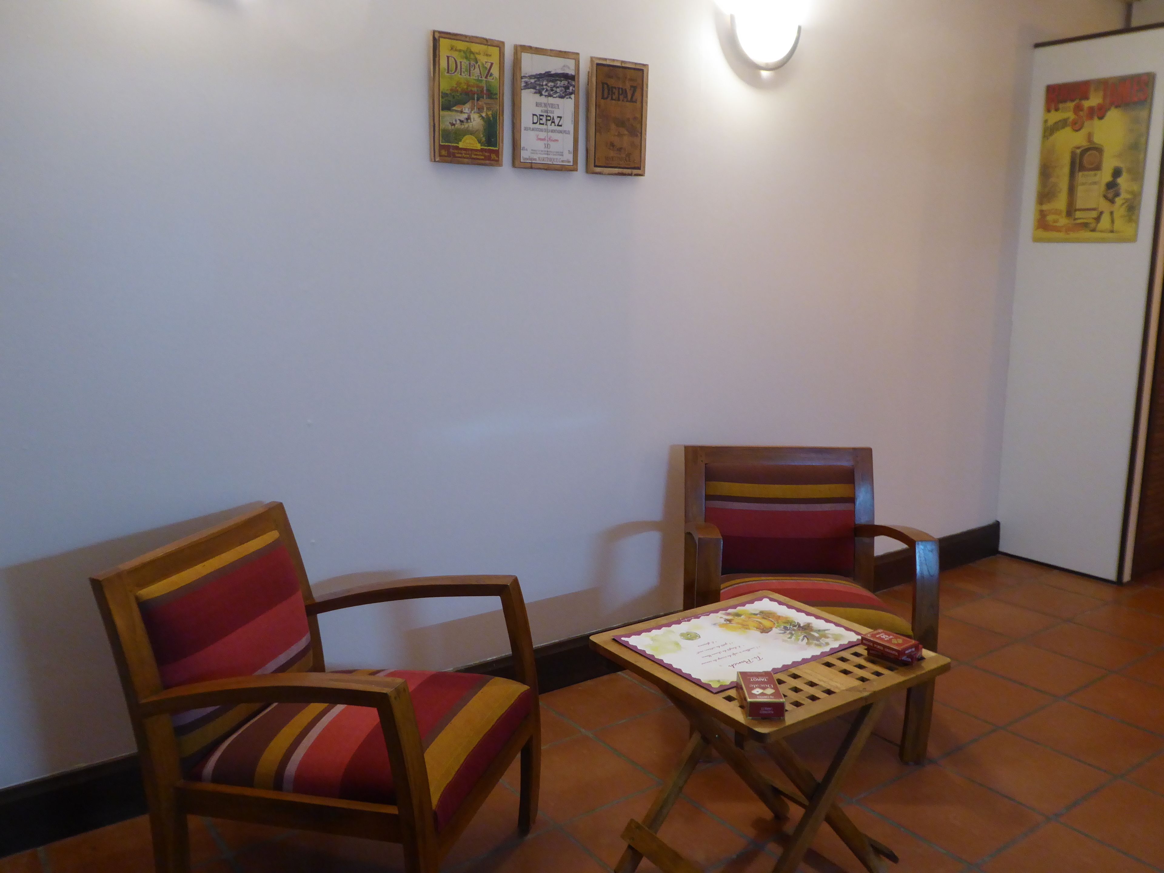 A room with two wooden chairs with striped cushions, a small wooden table with a certificate, and three framed posters on the wall.