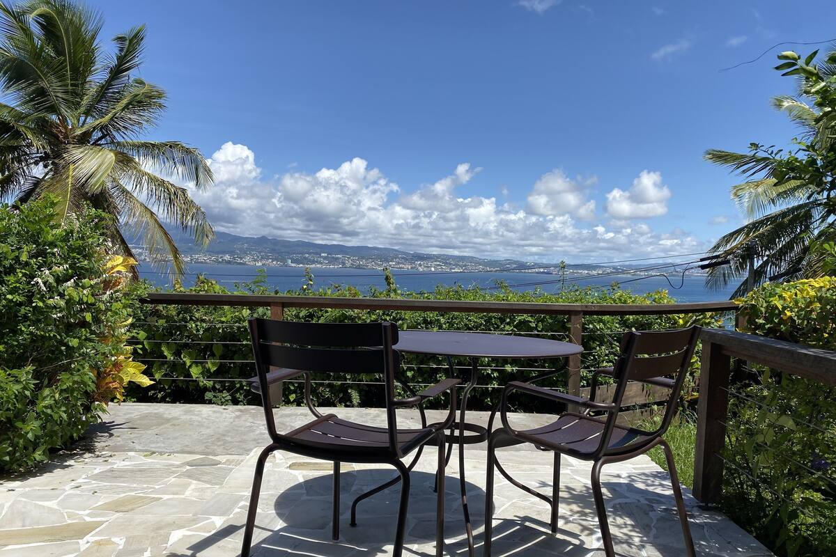 A patio with two metal chairs and a table, overlooking a scenic view of a coastal city and the sea.