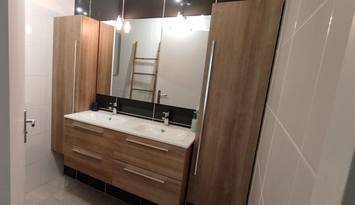 Une salle de bain avec un meuble-lavabo à deux vasques, des armoires en bois et un grand miroir.