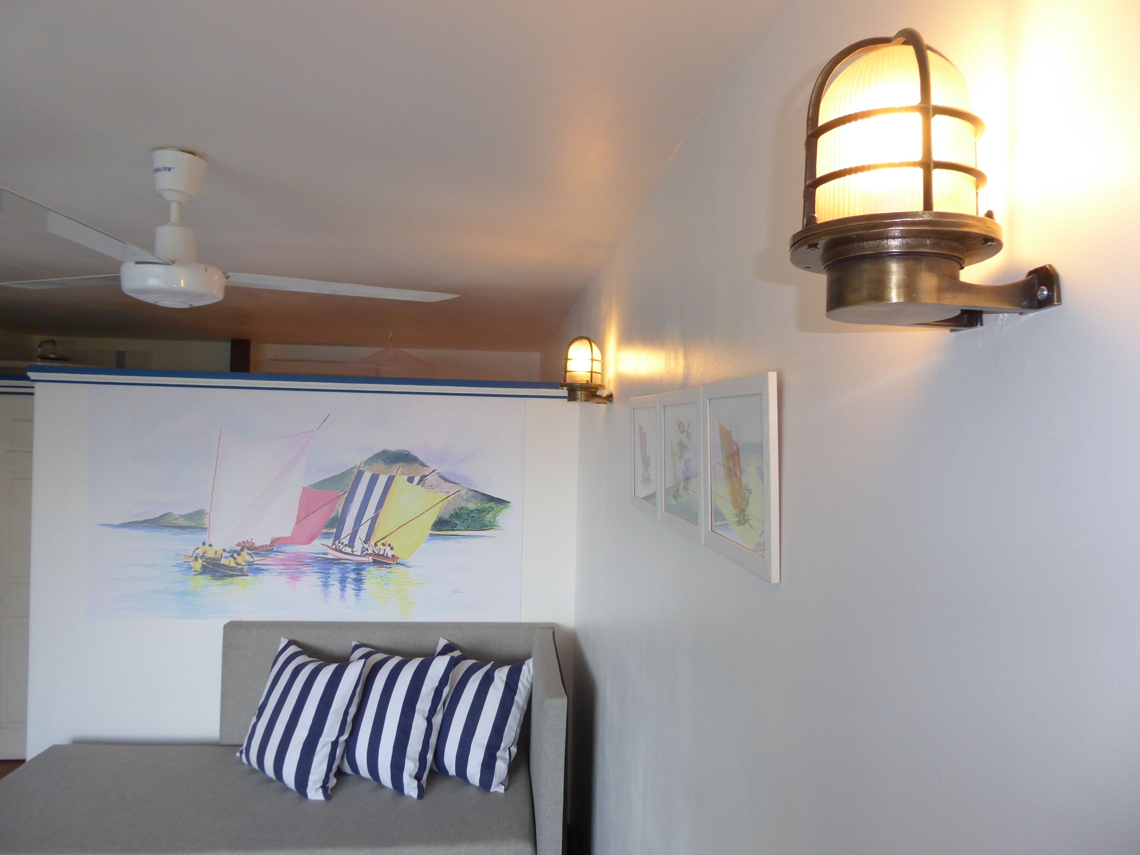 A bedroom with a bed, a ceiling fan, a wall-mounted lamp, and a large painting of a sailboat.