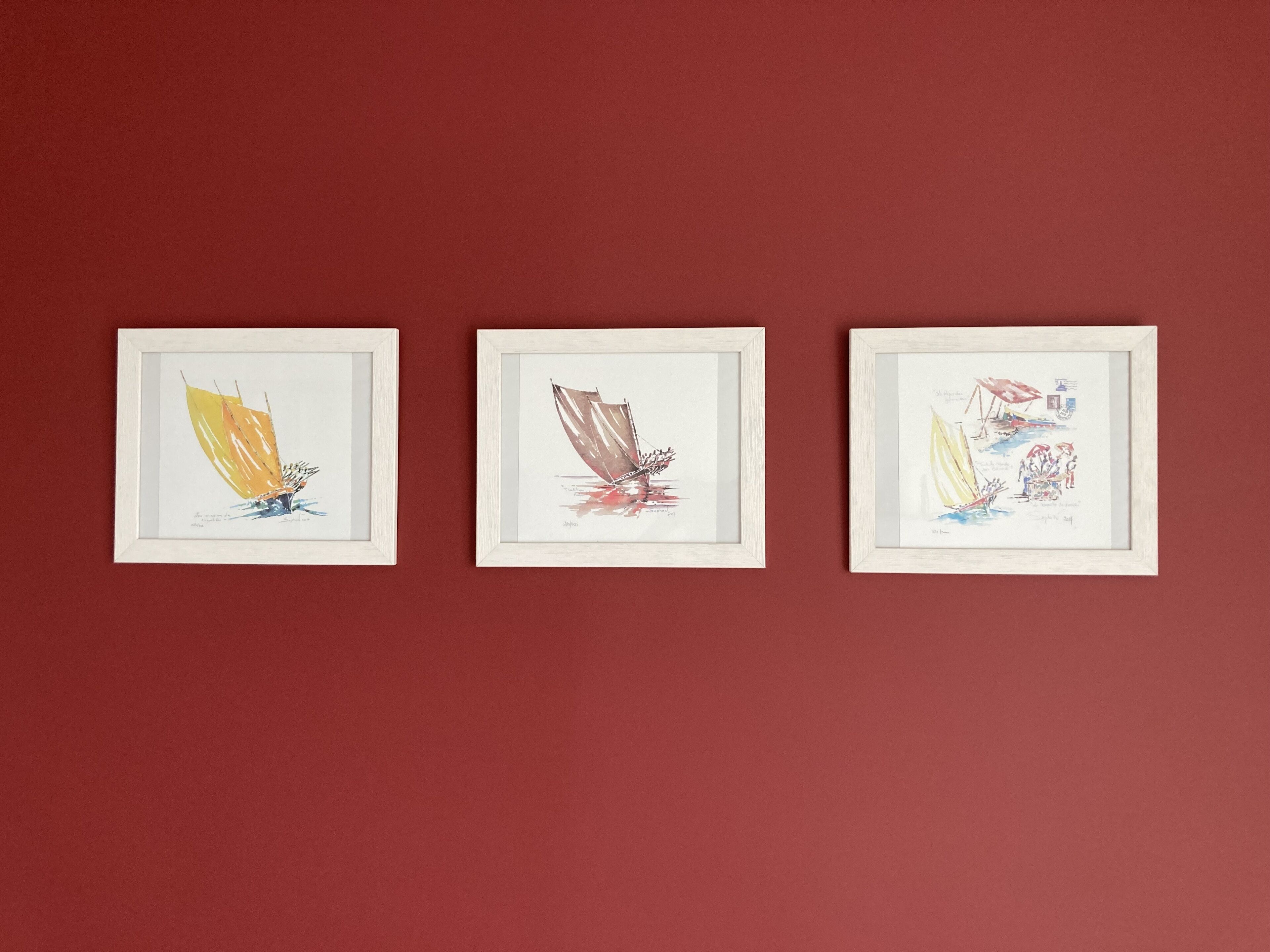 Tres obras de arte enmarcadas sobre una pared roja.