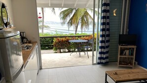 Eine moderne Küche mit Kühlschrank, Spüle und Kaffeemaschine. Ein Essbereich mit Tisch und Stühlen bietet Blick auf den Ozean und Palmen.