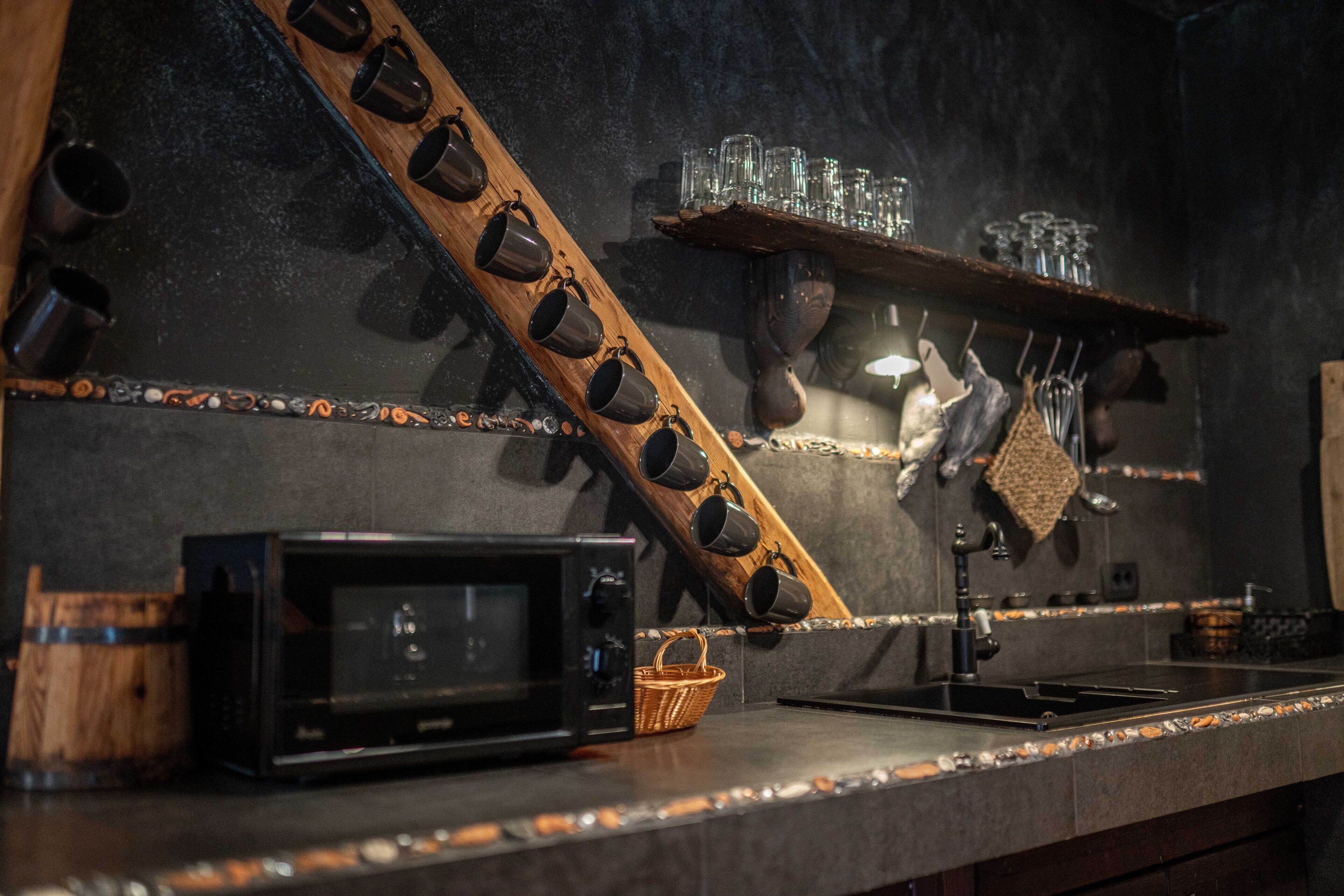 A kitchen with a microwave, a wooden rack with mugs, and a shelf with glasses.