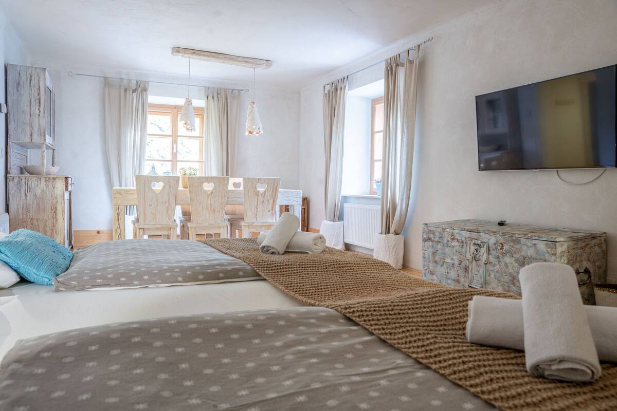 Ein Zimmer mit zwei Betten, einem Fernseher, einer Holzkommode und einem Fenster mit Vorhängen.