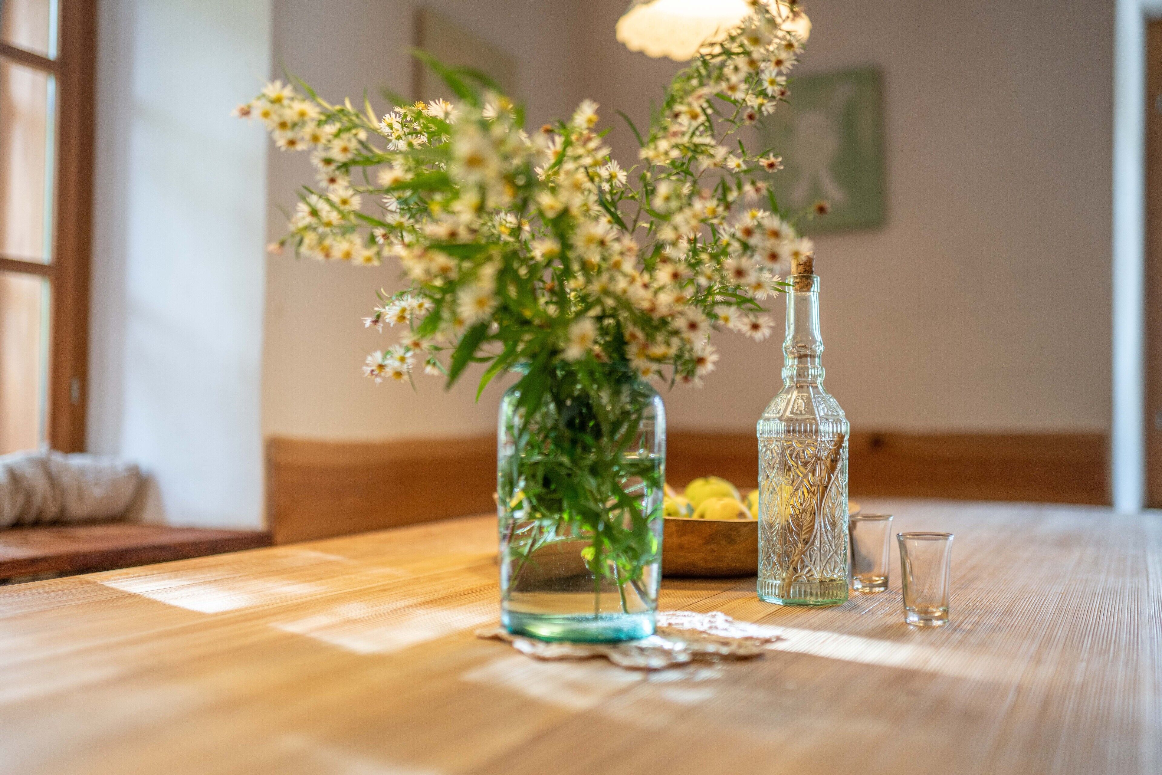 A wooden table with a glass vase containing white flowers and a decorative bottle.