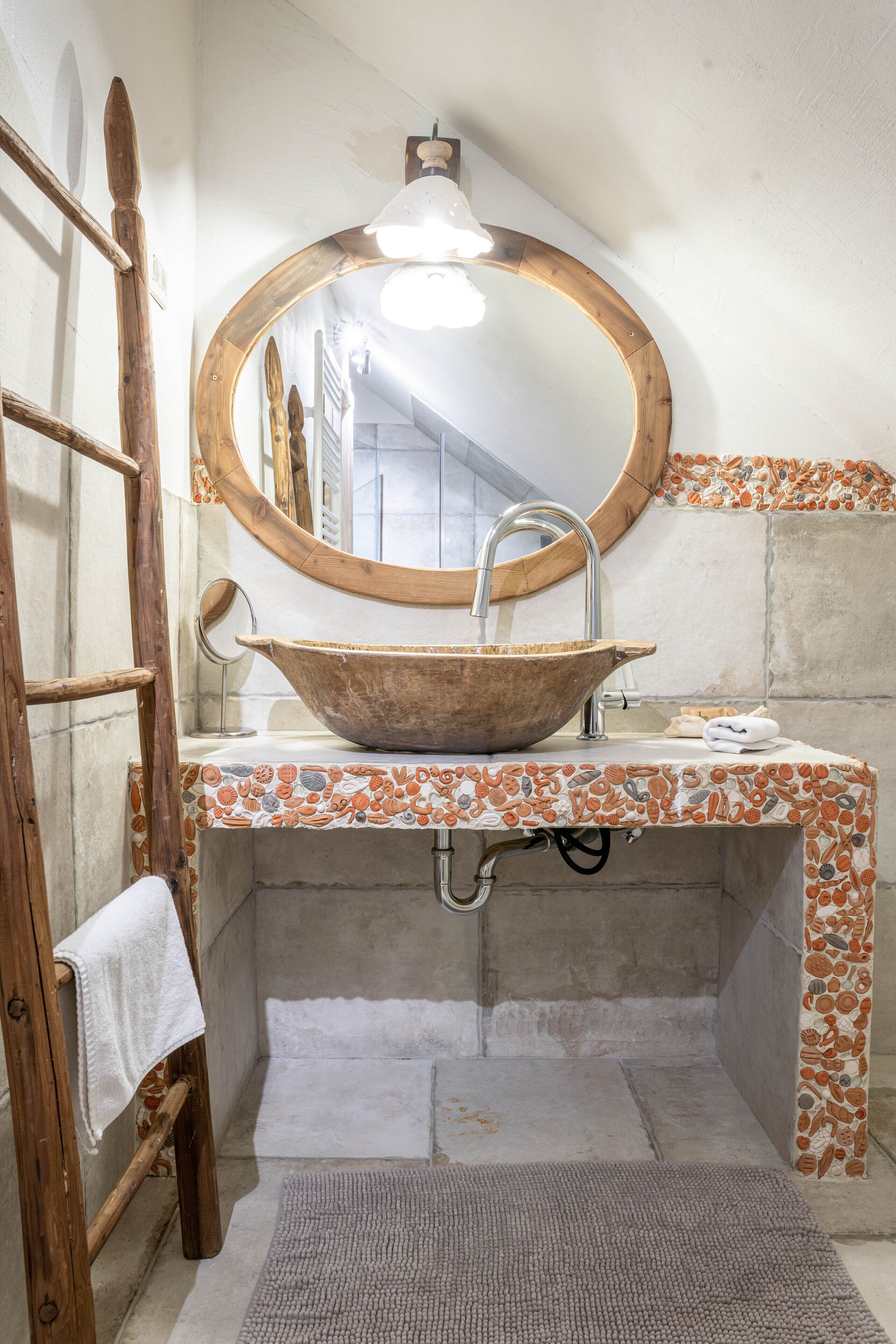A bathroom with a wooden bowl sink, a round mirror, and a towel hanging on a wooden ladder.