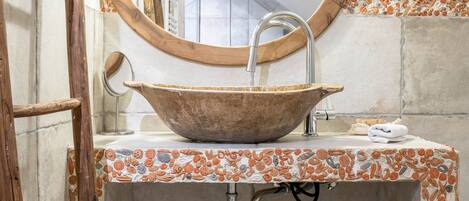A bathroom with a wooden bowl sink, a round mirror, and a towel hanging on a wooden ladder.
